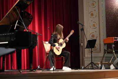 Dziewczyna gra na gitarze na scenie. Wokół stoją inne instrumenty.