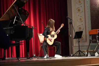Dziewczyna gra na gitarze na scenie. Wokół stoją inne instrumenty.