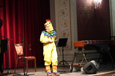 Chłopiec w stroju kurczaka na scenie. Wokół instrumenty muzyczne.