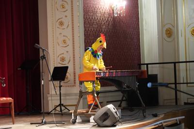 Chłopiec w stroju kurczaka gra na ksylofonie na scenie.
