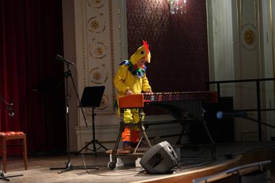 Chłopiec w stroju kurczaka gra na ksylofonie na scenie.