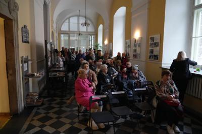 Grupa ludzi zebranych w korytarzu. Osoby z przodu siedzą, z tyłu stoją.