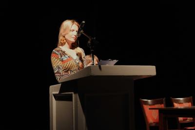 Pani przemawia przy mównicy do publiczności.