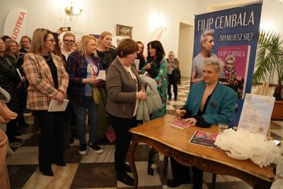 Kolejka czekająca na autograf na spotkaniu autorskim. Autor podpisuje egzemplarz książki.
