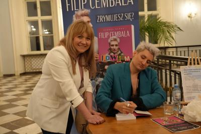 Spotkanie autorskie, autor składa autograf na egzemplarzu książki uśmiechniętej pani.