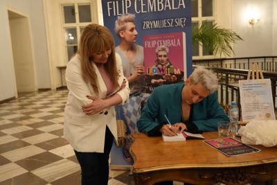 Spotkanie autorskie, autor składa autograf na egzemplarzu książki uśmiechniętej pani.