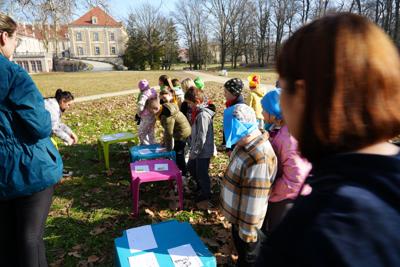 Dzieci na zewnątrz na stolikach rozwiązują zadania.