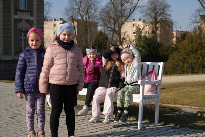 Grupa uśmiechniętych dziewczynek pozująca do zdjęcia obok ławki.