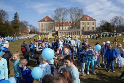 Grupa dzieci ubrana na niebiesko. W tle budynek pałacu.