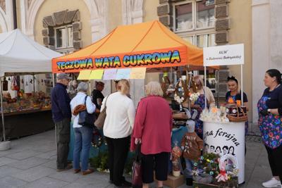 Grupa osób ustawiona przy stoisku z watą cukrową. Wokół dekoracje wielkanocne.