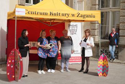Osoby stojące przy stoisku organizatora. Obejmują się.