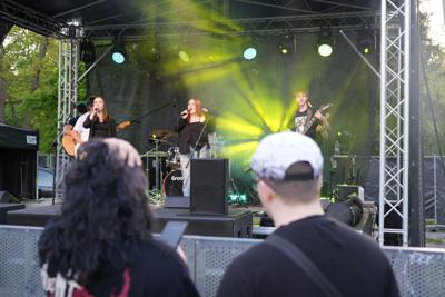 Osoby pod sceną oglądają występ grupy muzycznej.