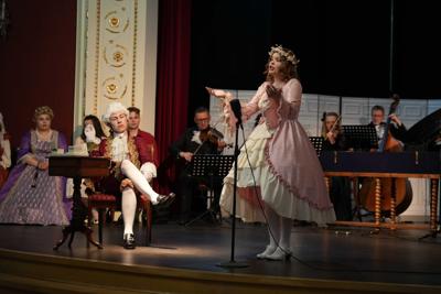 Osoby w historycznych przebraniach występują na scenie. Za nimi artyści grający na instrumentach.