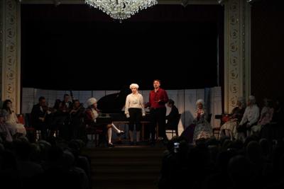 Artyści w historycznych przebraniach występują na scenie. Za nimi orkiestra.