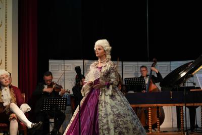 Artyści w historycznych przebraniach występują na scenie. Za nimi orkiestra.