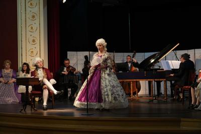 Artyści w historycznych przebraniach występują na scenie. Za nimi orkiestra.