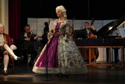 Artyści w historycznych przebraniach występują na scenie. Za nimi orkiestra.
