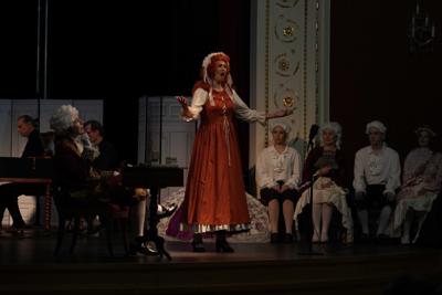 Artyści w historycznych przebraniach występują na scenie. Za nimi orkiestra.