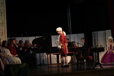 Artyści w historycznych przebraniach występują na scenie. Za nimi orkiestra.