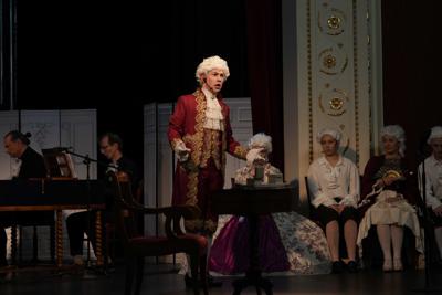 Artyści w historycznych przebraniach występują na scenie. Za nimi orkiestra.