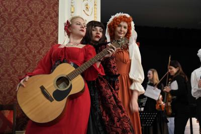 Osoby w historycznych przebraniach pozują z gitarą.