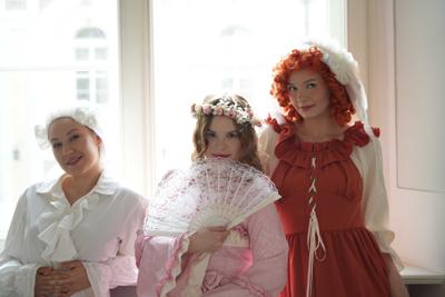 Osoby w historycznych przebraniach stoją pod oknem.