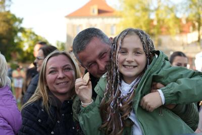 Uśmiechnięci państwo przytulający dziewczynkę.