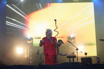 Pani w czerwonym garniturze śpiewa na scenie.