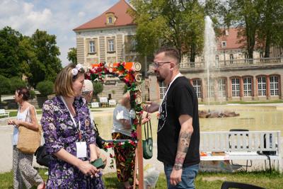 Dwie osoby rozmawiają, za nimi widać pałac.