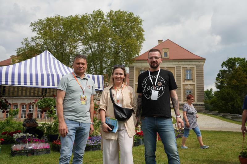 Osoby, za nimi widać stoisko z roślinami i pałac.