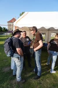 Trzech mężczyzn rozmawiających przy namiocie.