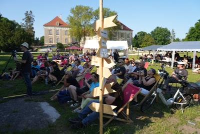 Drogowskaz, za nim grupa osób siedzących.