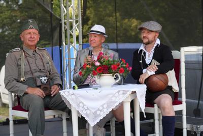 Trzech panów siedzących przy stoliku z dzbankiem z kwiatami.