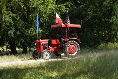 Pan jedzie drogą traktorem z flagami Polski, Unii Europejskiej i Stanów Zjednoczonych.