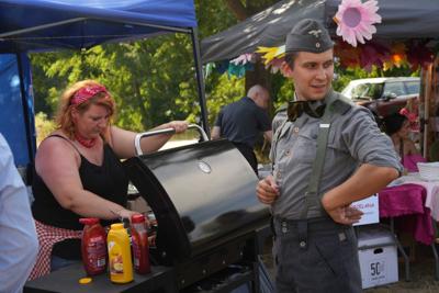 Pani przy grillu z kiełbaskami, przed nią pan w mundurze.