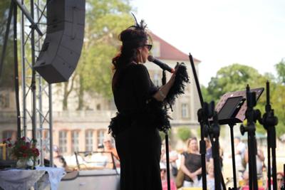 Pani śpiewa na scenie. W tle widać pałac i publiczność.