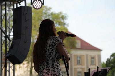 Artystka śpiewająca na scenie. W tle widać budynek.