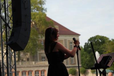 Artystka śpiewająca na scenie. W tle widać budynek.