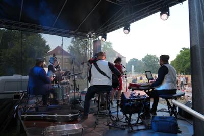 Grupa artystów występujących na scenie. W tle publiczność.