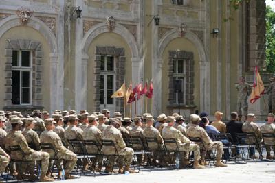 Grupa żołnierzy siedzi na placu, za nimi pałac.