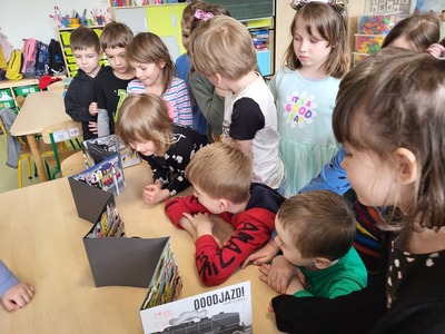 dzieci z zainteresowaniem oglądają książkę o pociągach 