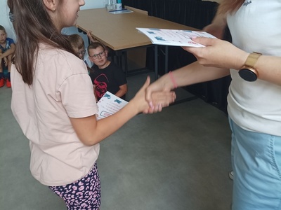 Dziecko odbiera certyfikat udziału w półkoloniach.