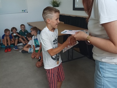 Dziecko odbiera certyfikat udziału w półkoloniach.