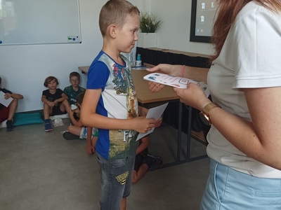 Dziecko odbiera certyfikat udziału w półkoloniach.