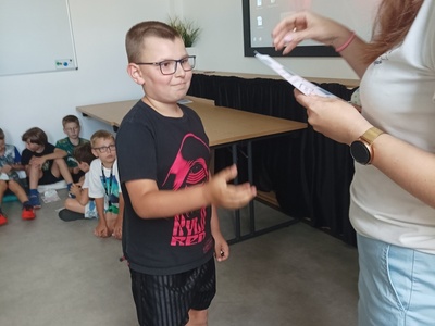 Dziecko odbiera certyfikat udziału w półkoloniach.