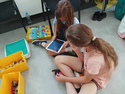 Dwie dziewczynki pracują na tablecie przygotowując zaproszenie dla rodziców na seans filmowy.
