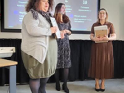 Trzy kobiety. Jedna wręcza podziękowanie.