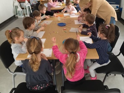 Dzieci ozdabiają szablon jajka wyciętymi z papieru elementami.