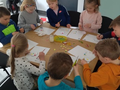 Dzieci ozdabiają szablon jajka wyciętymi z papieru elementami.
