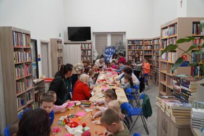 Walentynkowa niespodzianka. Praca wre. Dzieci siedząc przy stołach pośrodku biblioteki, wykonują prace plastyczne pod kierunkiem pań prowadzących z Klubu Seniora w Gościeradowie.